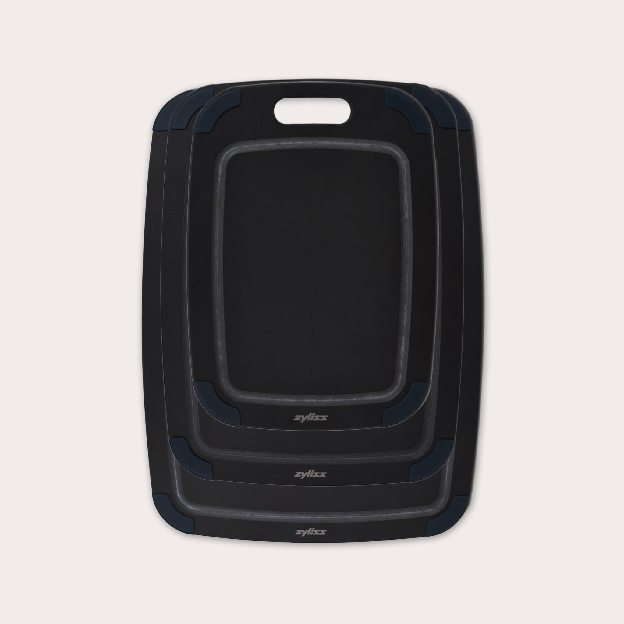 The Zyliss Wood Fibre Cutting Boards set features three nested black boards in different sizes, each with a handle slot and dark gray corner grips, made from eco-friendly recycled wood fibres and shown on a light background. #set of 3