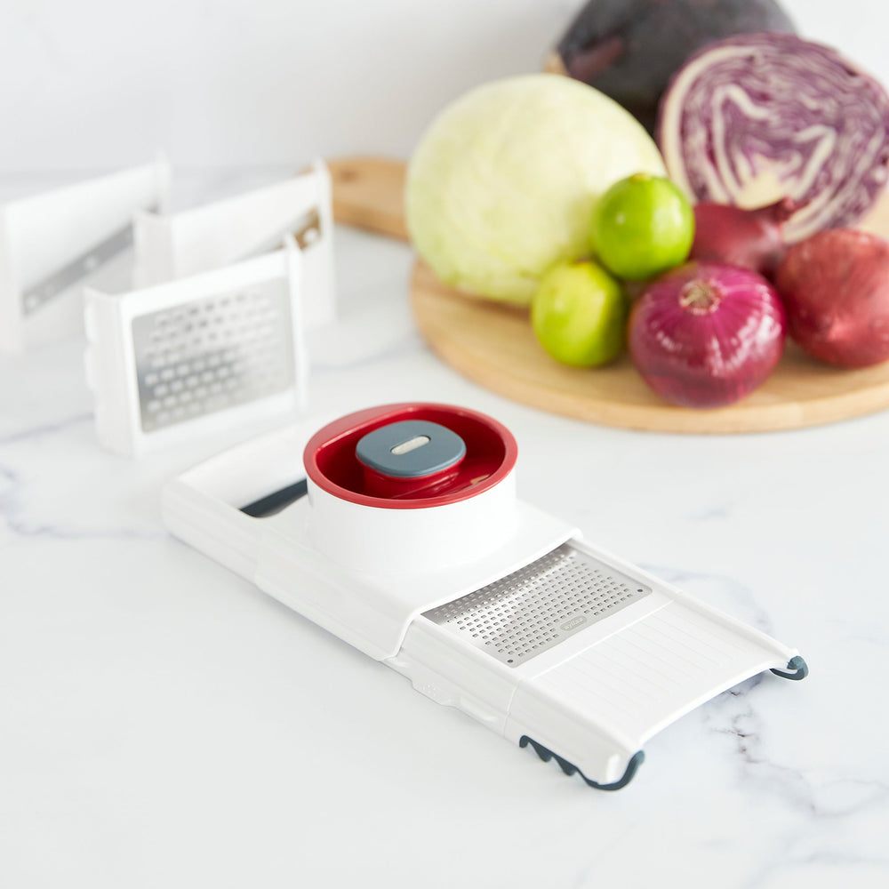 The Zyliss 4-in-1 Slicer & Grater in white and red, with a stainless steel blade and hand guard, sits on a light background—ideal for fast slicing or grating in any kitchen.