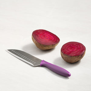 A Zyliss 6 Piece Knife Set stainless steel knife with a purple handle rests beside a halved beet, displaying its vibrant red interior—ideal for food prep on a light surface.