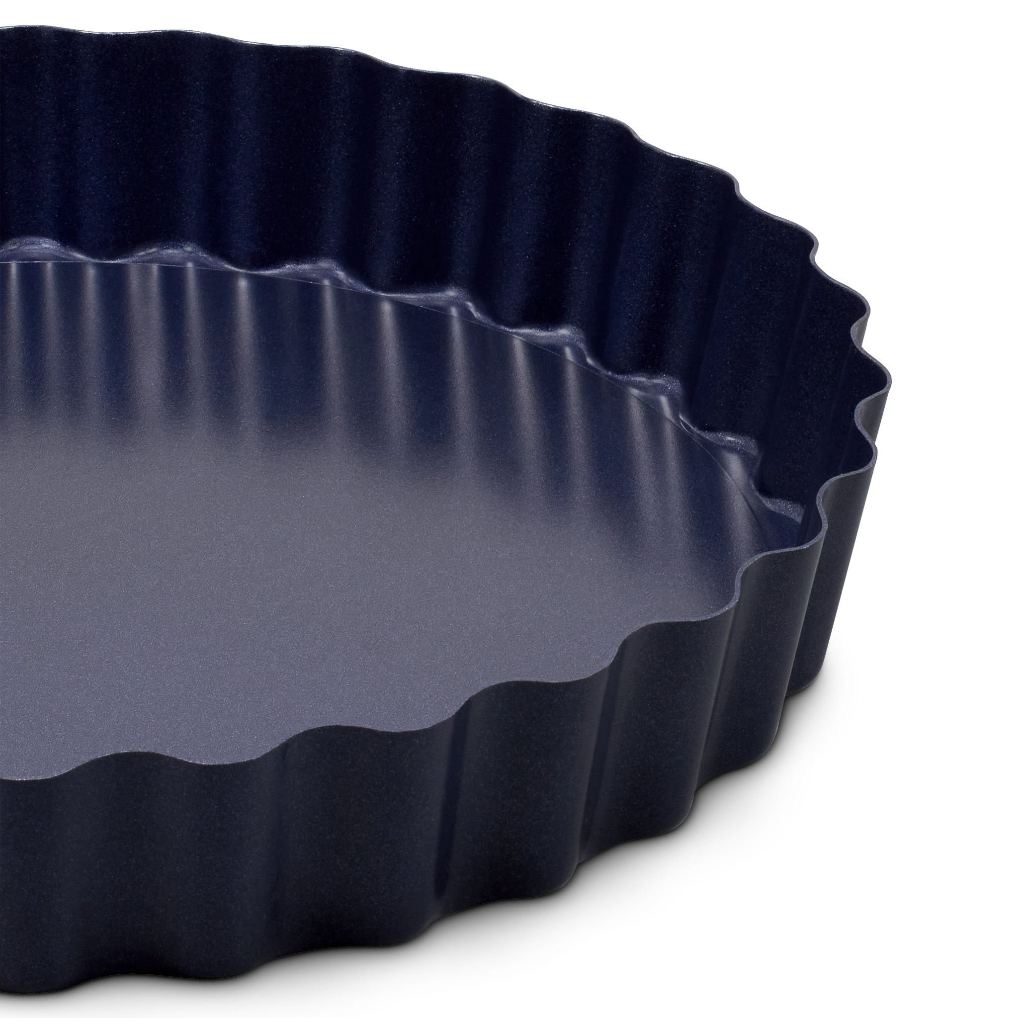 Close-up of a dark nonstick tart pan with a wavy, fluted edge and smooth interior surface, shown on a white background.