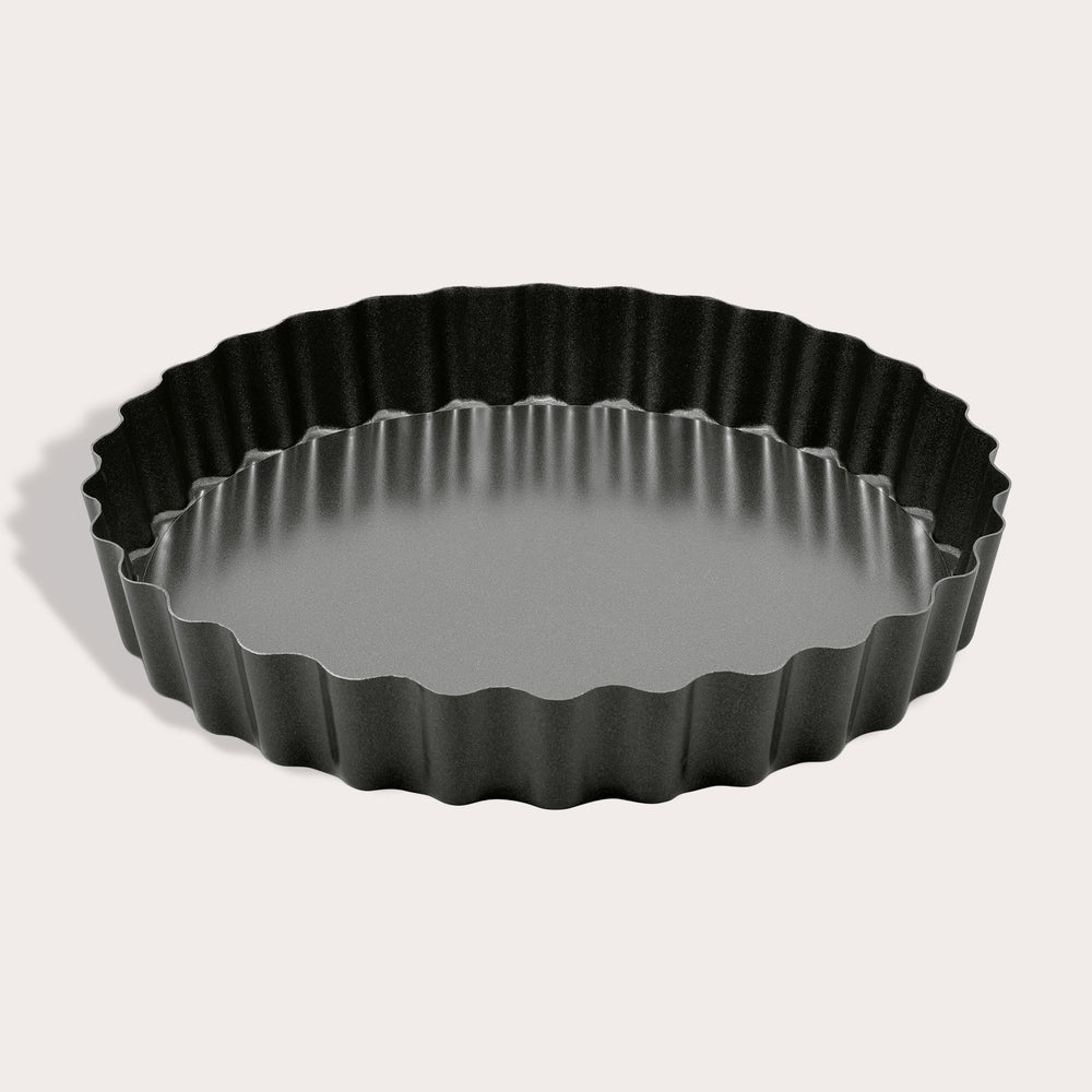 The Zyliss Non-Stick Tart Pan is round and black with fluted edges, a flat bottom, and a removable base—ideal for baking tarts or quiches. The empty pan is displayed on a light background.