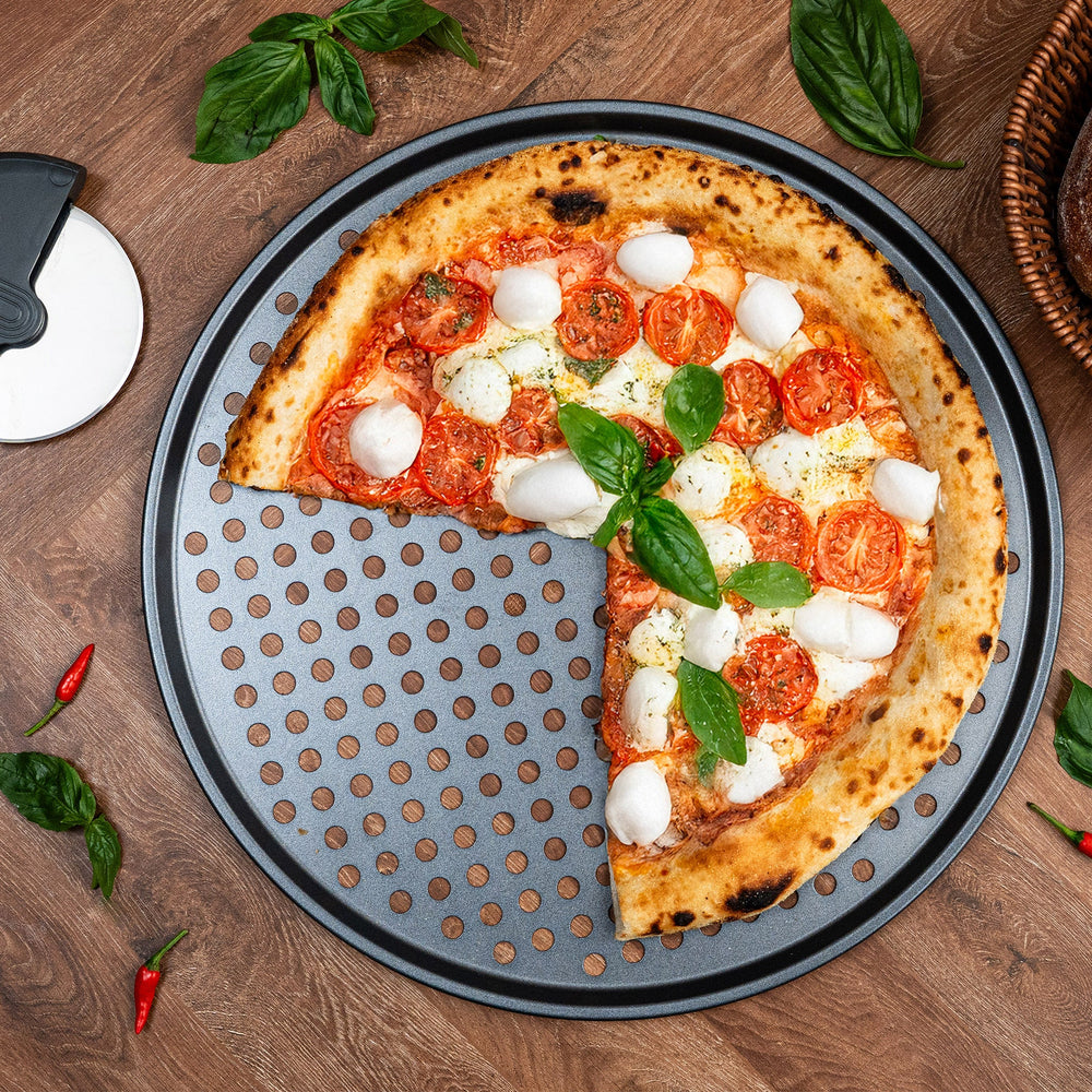 The Zyliss Non-Stick Pizza Tray is a round, black, carbon steel tray featuring numerous evenly spaced holes for crispy pizza bases. Shown on a white background.
