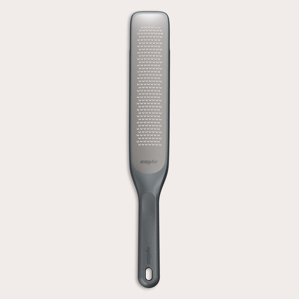 The Zyliss Rasp Grater is a long, rectangular foot file with a gray handle and textured metal surface for removing calluses and dead skin. The handle features a hanging hole for easy storage. 
