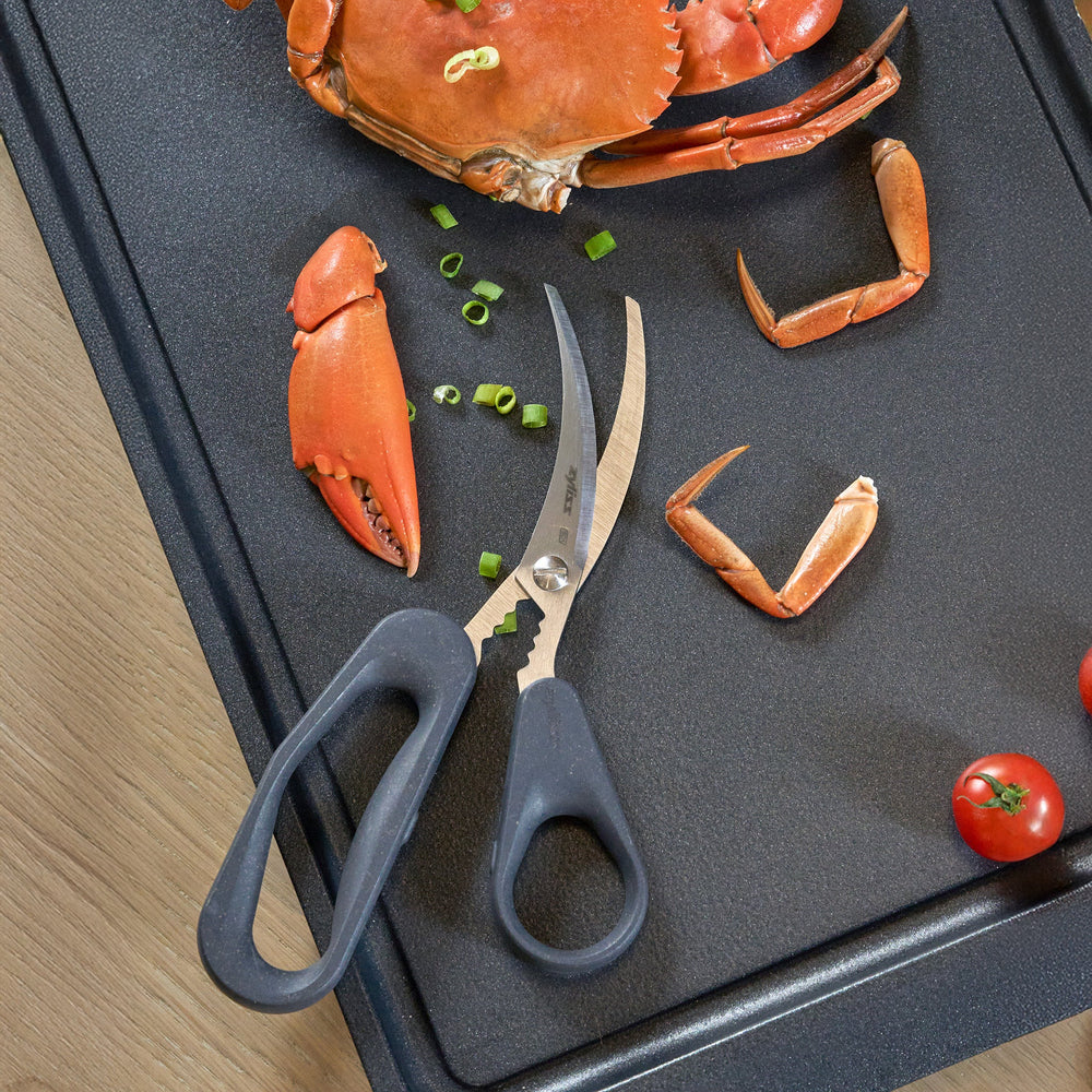 Zyliss Seafood Scissors with black ergonomic handles and a curved, partially serrated stainless steel blade are displayed against a light beige background, designed specifically for shellfish preparation.