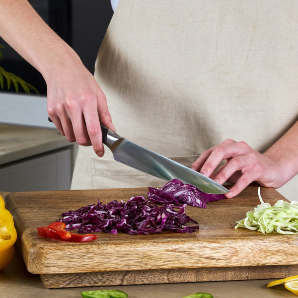 A person uses the Zyliss Comfort Pro Carving Knife 20cm/8" with an ergonomic handle to slice purple cabbage on a wooden cutting board, which also holds chopped green cabbage and red and yellow bell pepper pieces.