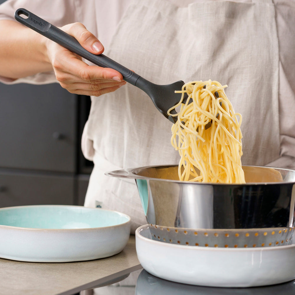 The Zyliss Spaghetti Server is a black, heat-resistant utensil with a long handle and slotted, rounded head featuring prongs for ideal portion control, shown isolated on a light background. 