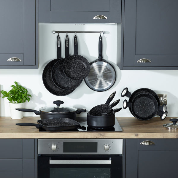 A modern kitchen with gray cabinets and a wood countertop features Zyliss Ultimate Non-Stick Frying Pans in black speckle, some hanging on a wall rack, others on the stove and counter. A potted basil plant sits to the left. #2Pc_Set